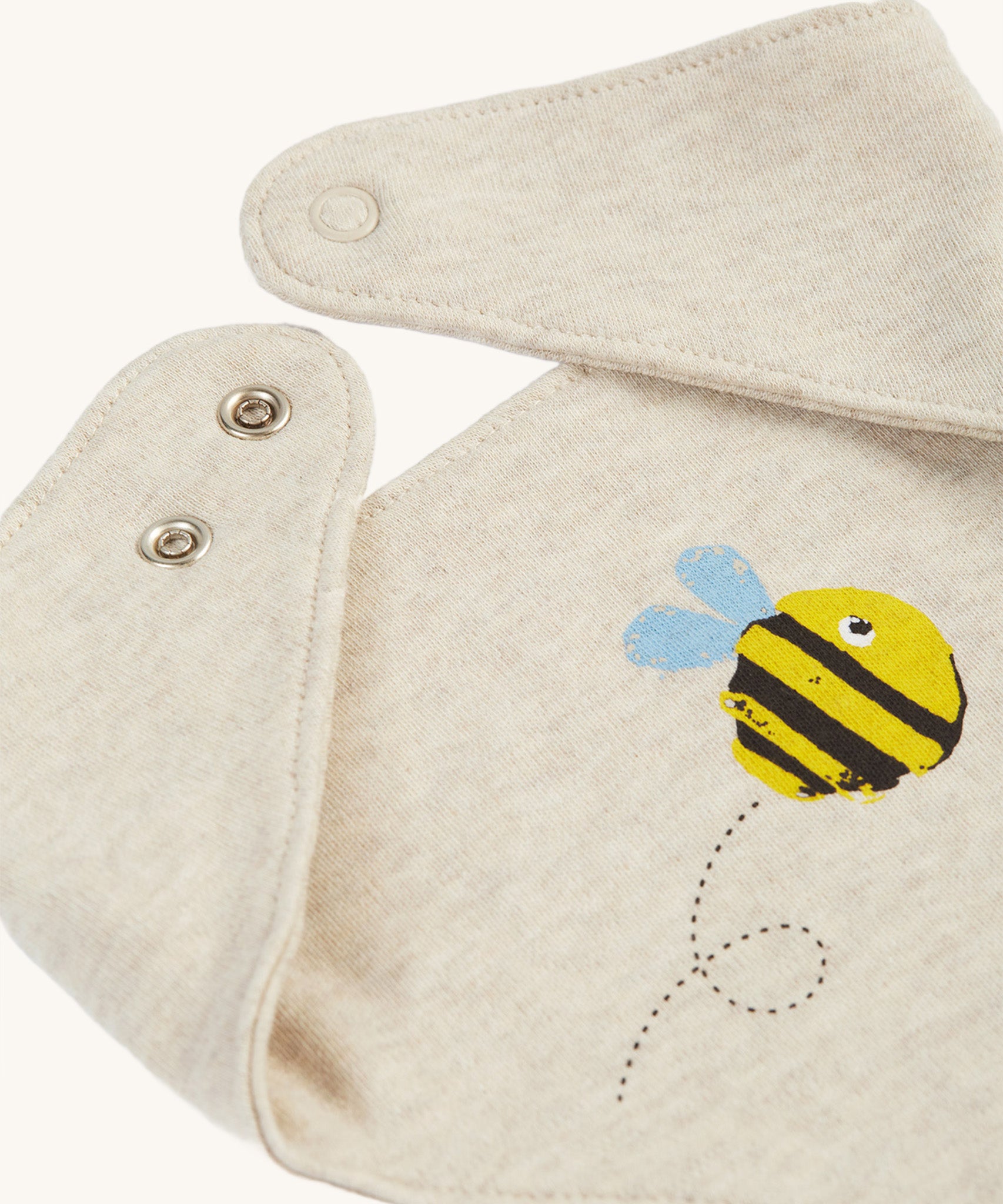 A closer look at the bib on the Frugi Baby Gift Set - Buzzy Bee. A dark cream cotton fabric, with a buzzy bee on the front