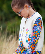 A close up of a girl wearing the Frugi Oatmeal Flowers Connie Cotton Knitted Sleeveless Cardigan available at Babipur showing  the embroidery detail.