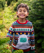 A child standing in a forest and wearinf the Frugi forest fairisle/yeti jumper available at Babipur. A GOTS organic cotton jumper with a cute playful yeti on a festive fairisle design. Features a button fasteners on the shoulder