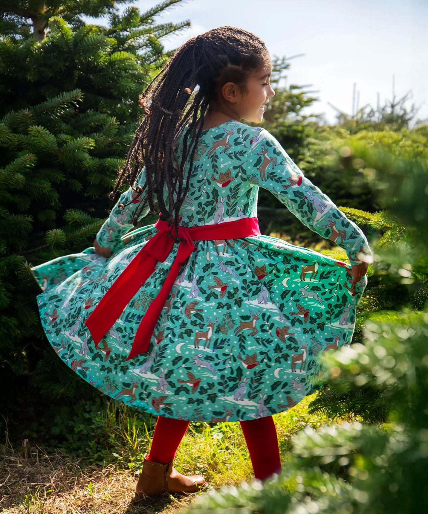 The back of a child wearing the Frugi party skater dress in festive forest available at Babipur showing the red tie around the waist and tied in a festive inspired bow.