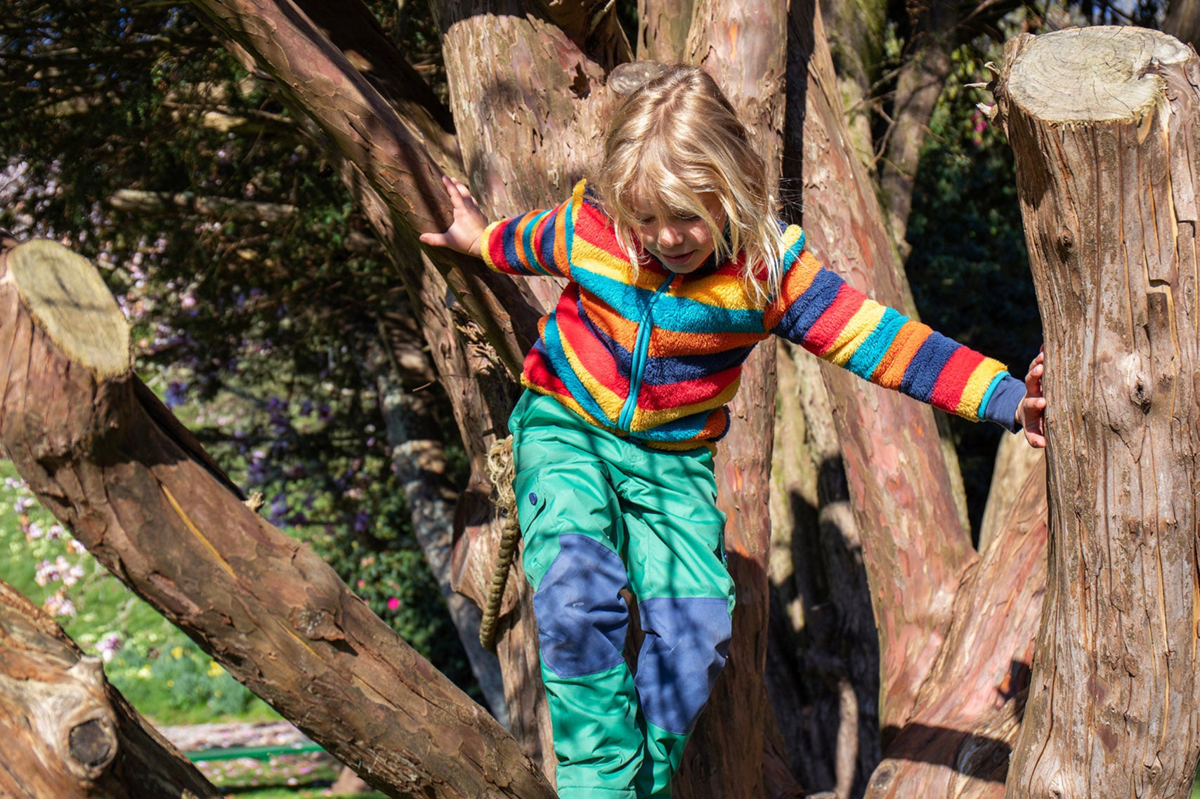A child Playing in the trees and wearing the Frugi Autumn stripe ted fleece available at Babipur.. A long sleeve striped thick fleece with light blue trim and turn up collar.