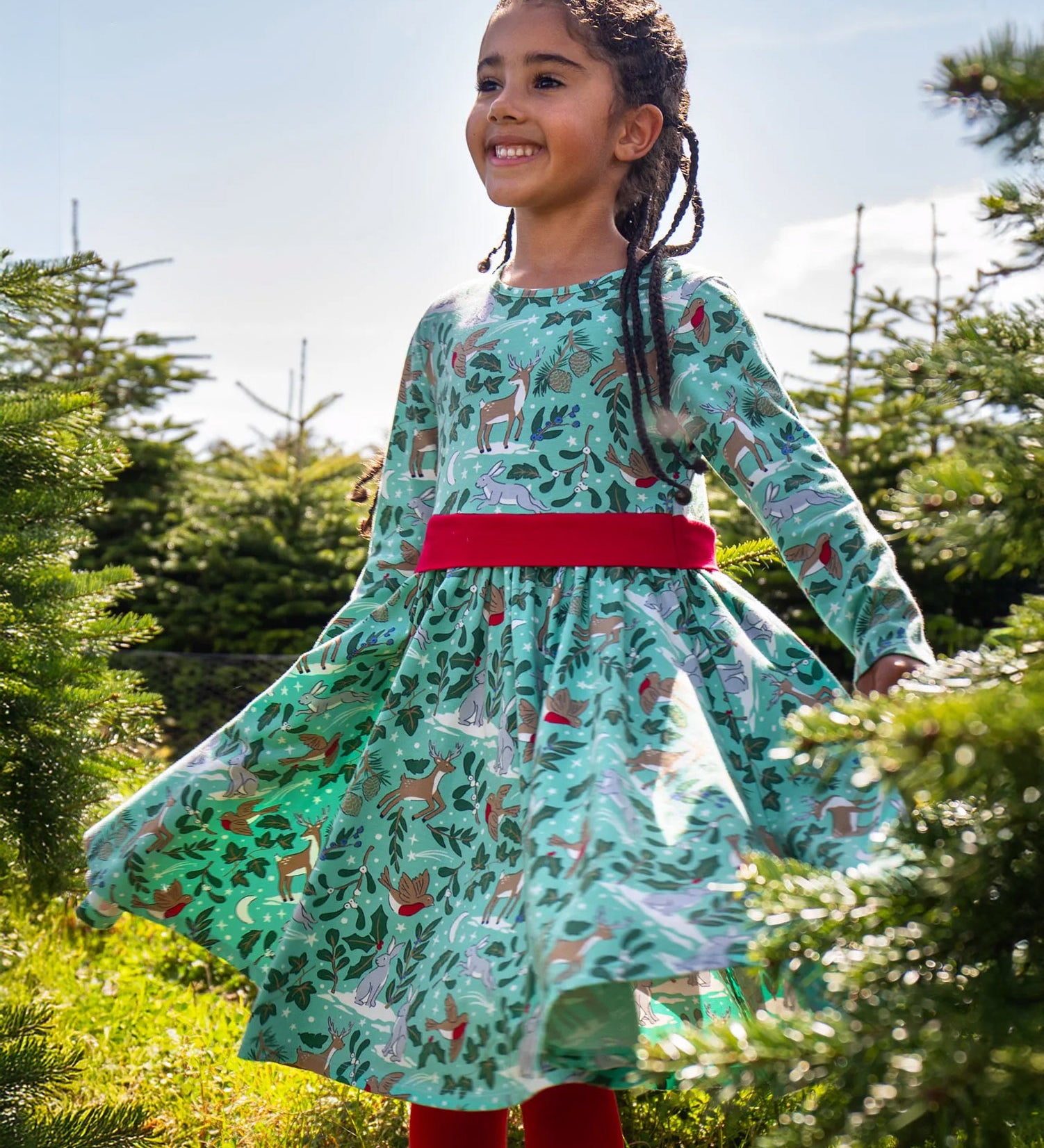 A child standing in the middle of a forest and wearing the the Frugi party skater dress in festive forest available at Babipur showing the gather of the dress
