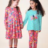 A child wearing the Frugi sofia skater dress in tulip/fun flowers and standing next to another child wearing the tulip fun flowers leggings with the Frugi dragon stripe/bee top available at Babipur