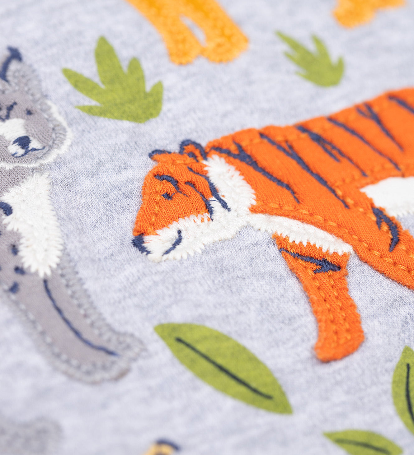 A close up of the orange tiger applique on the front of the Frugi Jake Grey Big Cats Circular Organic Cotton Long Sleeved Kids' Top. The top has four big cat and leafy themed appliques on the front. This top is a part of a wide range of organic cotton clothing for children available here at Babipur.