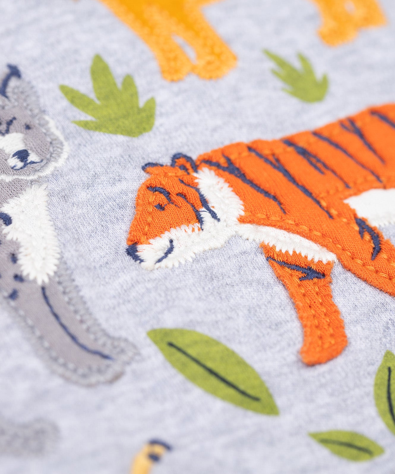 A close up of the orange tiger applique on the front of the Frugi Jake Grey Big Cats Circular Organic Cotton Long Sleeved Kids' Top. The top has four big cat and leafy themed appliques on the front. This top is a part of a wide range of organic cotton clothing for children available here at Babipur.