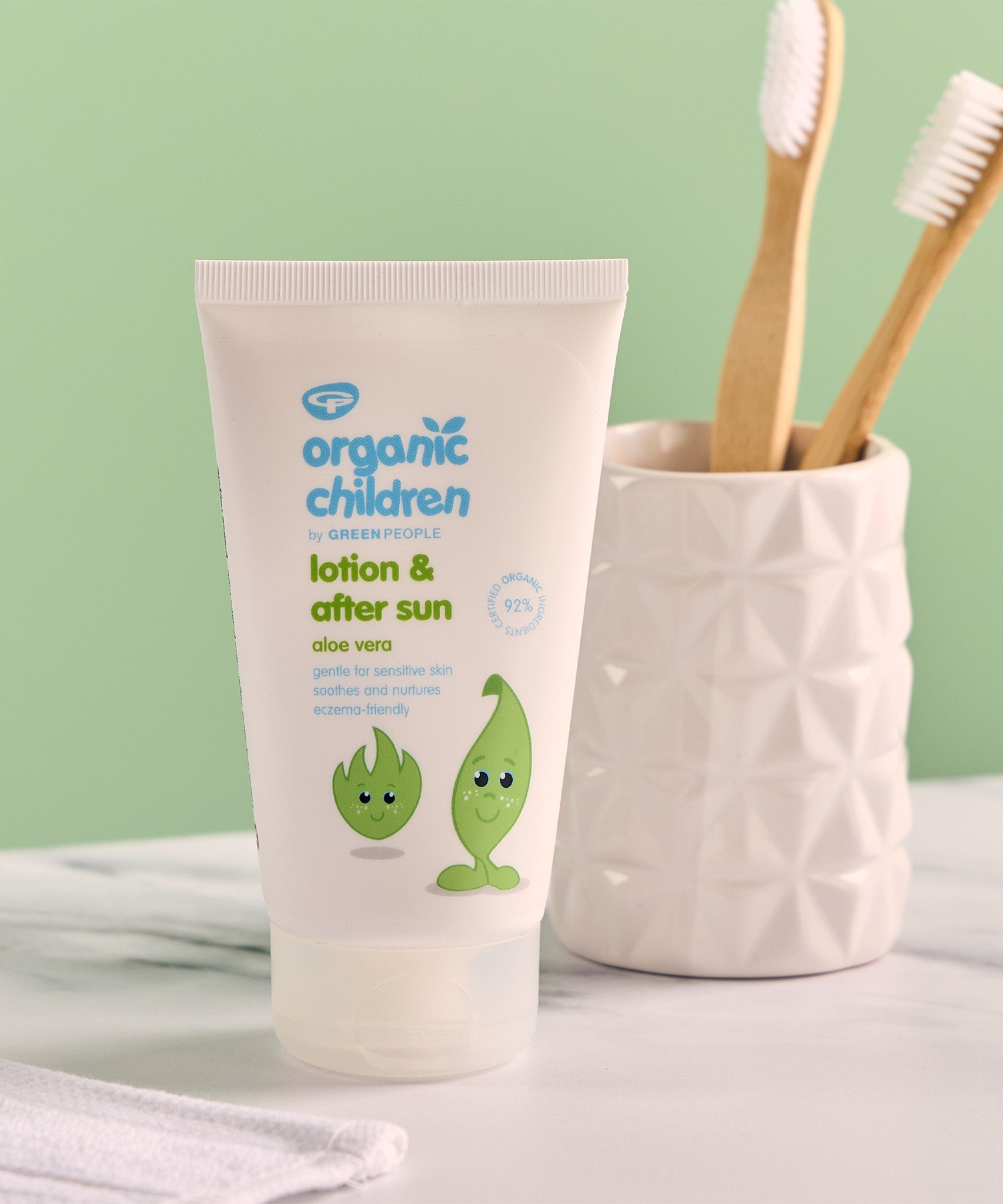 Green People organic children's aloe vera lotion & aftersun in 50ml bottle standing on a stone surface next to a toothbrush holder