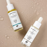 The Green People Nordic Roots Hyaluronic Booster Serum and Nordic Roots Marine Facial Oil laid on a peach coloured background with water droplets, to represent the hydrating nature of the products