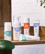 The full collection of the OY! Organic Young skincare range which includes deodorant, face wash, moisturiser, concealer and serum. All the items are stood on a wooden shelf, with a white backgorund