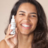 A person with a big smile on their face, holding the Green People Nordic Roots Hyaluronic Booster Serum in their hand