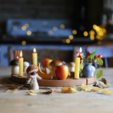 A beautiful Autumnal display made using a Grimm's Wooden Celebration Ring. little leaves are scattered in front of the ring, with colourful decoration and candles in the little holes.