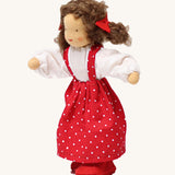 Grimm's Brown Haired Girl Doll - Lana, has brown hair and is wearing a white top under a red dress with white spots all over and is Waldorf inspired. The image is on a cream background