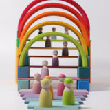 Grimm's 12 Pastel Friends stood on colourful pastel Grimm's blocks and rainbow arches. The image shows the Grimm's Pastel friends in the foreground and in the backgrund stood on Grimm's wooden pastel coloured slats, underneath the rainbow arches