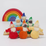 The Grimm's Rainbow Dwarfs collection showing a red, orange, yellow, light blue, green and indigo Grimm's Rainbow Dwarfs on natural wood blocks, with a mini Grimm's rainbow in the background