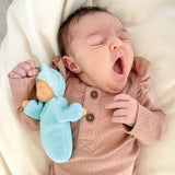A small baby is yawning whilst sleeping, and is cuddles with Grimm's Lavender Doll Aqua