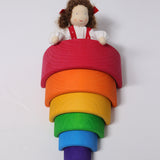 Grimm's Brown Haired Girl Doll - Lana is laid under a Grimm's Wooden rainbow with its hands on top of one of the rainbow arches