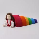 Grimm's Brown Haired Girl Doll - Lana is laid underneath a Grimm's Wooden Rainbow and is propped up on its arms and bend backwards slightly at the waist
