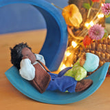 Mr Ebony and Baby Leo are playing on a light blue piece of a Grimms wooden toy. There are flowers and fairy lights in the background