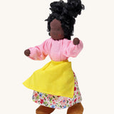 Grimm's Handmade Doll - Mrs Ebony, is a lovely female character doll with black skin, a smiling face, long curly black hair, a pink top and flowery skirt, a yellow apron and light brown fabric shoes. The image is on a cream background
