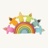 The Grimm's Pastel Dwarfs toy dolls sat on top of a grimm's small wooden pastel rainbow toy, on a cream background