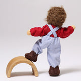 A behind shot of Grimm's Brown Haired Doll - Peter with its foot resting on a piece of Grimm's natural wooden rainbow. This image shows the flexibility of the dolls limbs