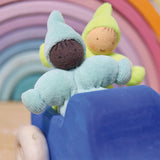 The pastel blue and pastel green The Grimm's Pastel Dwarfs dolls are sat in a wooden blue Grimm's car toy, with a Grimm's pastel rainbow in the background