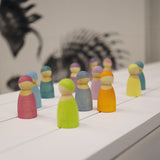 The Grimm's 12 Pastel Friends are all stood together on a white wooden table, with a black art silhouette in the background