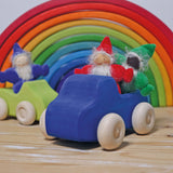 The red, green and indigo Grimm's Rainbow Dwarfs are sat in Grimm's wooden car toys with a large Grimm's rainbow in the background