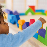 A child carefully puts a block on top of a wall they have created using the Grimm's Basic Building Set