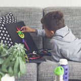 A child laying on a sofa, creating art with the Grimm's Small Magnetic Blackboard and some Grimms puzzle pieces