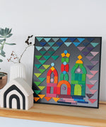 A colourful puzzle piece art work, on the Grimm's Small magnetic blackboard. In front of the board is a Grimm's monochrome house and a white vase with dried flowers in it