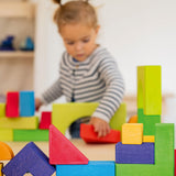 A child is happily playing with the Grimm's Basic Building Set in the back ground, with some of the Grimm's Basic Building Set Blocks in focus at the front