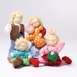 The Grimm's Waldorf Dolls Family are all together, and on a grey background. The family are Grimm's Blond Haired Woman Doll, Grimm's Blond Haired Girl Doll, Baby Mia,  Blonde Haired Male Doll and Blonde Haired Boy Doll - Linde.