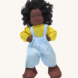 Grimm's Handmade Doll - Max is a lovely soft body doll. Max has curly black hair, black skin, a smiling face, a yellow top, light blue dungarees and brown shoes. The image is on a cream background