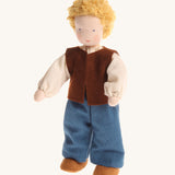 Grimm's Waldorf Blond Haired Man Doll has a soft body, blonde hair, blue eyes and is wearing light brown fabric shoes, blue trousers, a cream top and a dark brown sleeveless jacket. The image is on a cream background