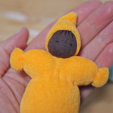 The yellow Pastel Dwarf Doll in a persons hand. A closer view of the pastel yellow Grimm's Pastel Dwarf, in a persons hand. The image shows the dwarfs body, smiling face and hat up close and gives a size guide as it fits in the palm of an adults hand.
