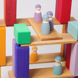A closer view of the Grimm's 12 Pastel Friends wooden peg dolls, standing on natural wooden Grimm's building boards and colourful blocks