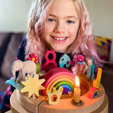 A child is celebrating their 8th birthday and has in front of them, a Grimm's Waldorf celebration ring filled with Grimm's decorative figures, a candle and a Grimm's number 8. In the centre is a Grimm's 6 piece mini wooden rainbow.