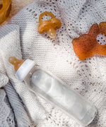 Hevea glass baby bottle, natural rubber dummy and teether on a white crochet blanket.