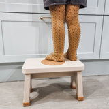Child in yellow tights stood on a Hevea Rubberwood Step Stool at a kitchen counter.