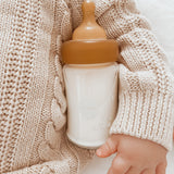 Baby wearing a cream jumper asleep with a Hevea Glass Baby Bottle