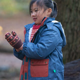 Child in a forest wearing a Kids Warm Waterproof Winter School Coat in a Moonlight Blue print with deep red details down the zip and on the front pockets, PFC Free, by Little Green Radicals, made from recycled bottles and a cosy polyester fleece, buy now at Babipur.