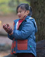 Child in a forest wearing a Kids Warm Waterproof Winter School Coat in a Moonlight Blue print with deep red details down the zip and on the front pockets, PFC Free, by Little Green Radicals, made from recycled bottles and a cosy polyester fleece, buy now at Babipur.