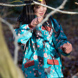 Girl stood in a forest wearing a Warm and Waterproof (5000M rating), PVC free kids school coat by Little Green Radicals, in a Winter Rabbit blue print, with red front pockets, buy now at Babipur.