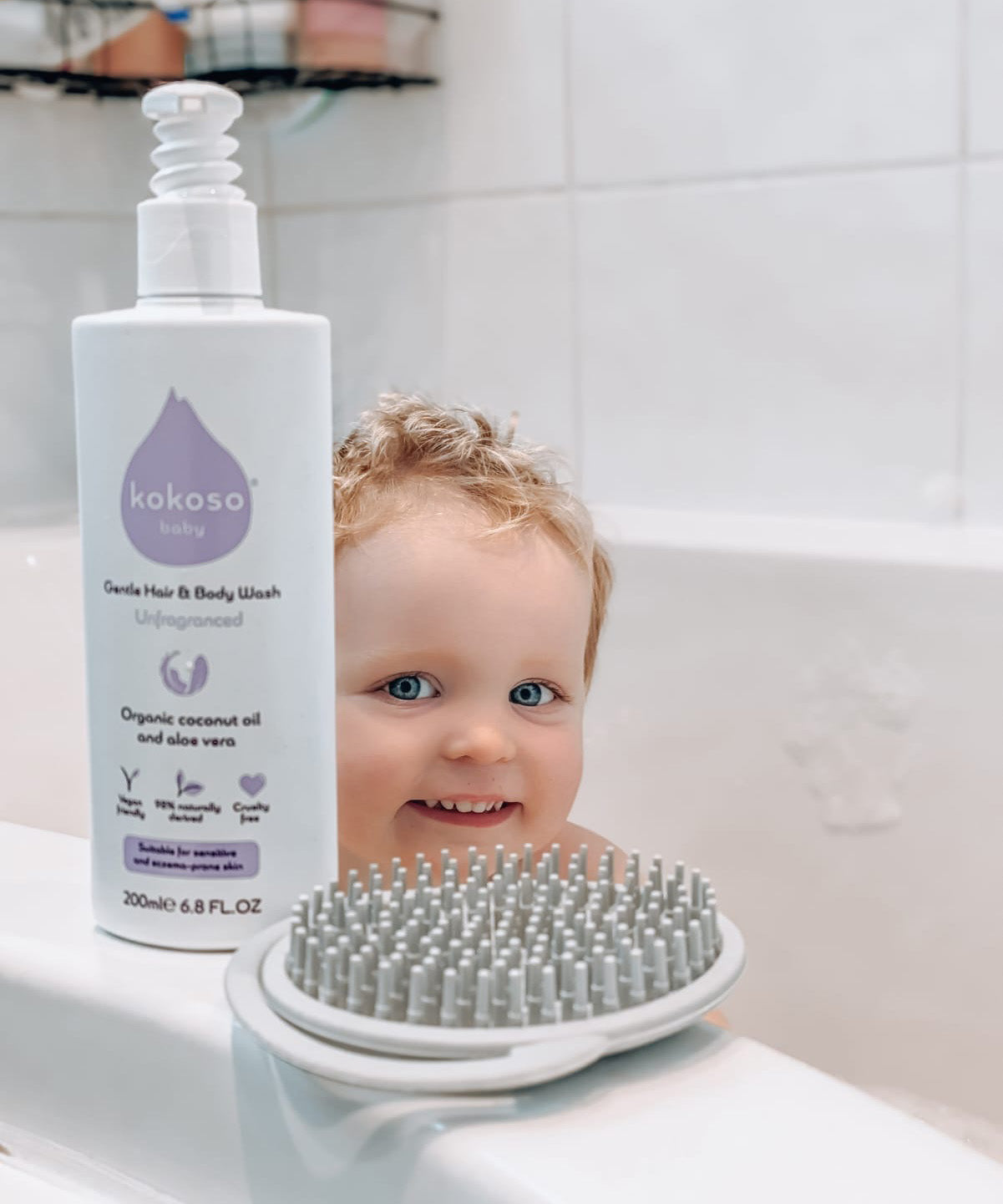 Kokoso unscented organic baby body and hair wash 200ml bottle standing on the side of the bath with a baby inside. Bottle available at Babipur