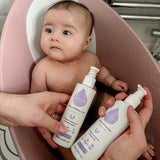 An adult hand holding the Kokoso unscented organic gentle hair & body wash and the baby lotion above a baby in a bath. Both are available at Babipur.