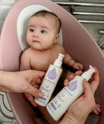 An adult hand holding the Kokoso unscented organic gentle hair & body wash and the baby lotion above a baby in a bath. Both are available at Babipur.