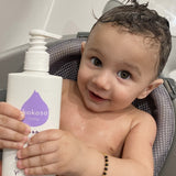 A close up of a baby holding the Kokoso unscented organic baby body and hair wash 200ml bottle. Bottle available at Babipur.