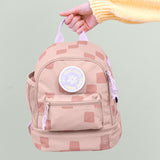 A adult hand holding the Lassig kids mini pattern party rose pattern backpack by the lilac handle on the top of the backpack