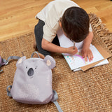 A child sitting on a rug, drawing next to the Lassig koala tiny backpack.