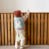 A small child standing near a wooden fence and wearing the Lassig kids tiny backpack in penguin